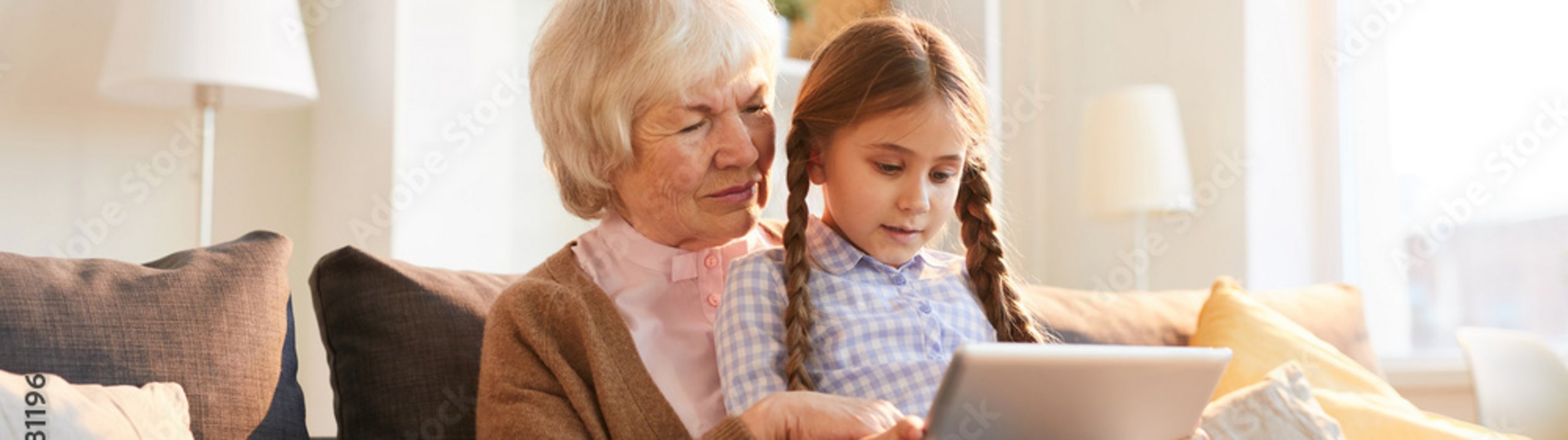 Großmutter und Kind sitzen auf dem Sofa und schauen gemeinsam auf ein Tablet.