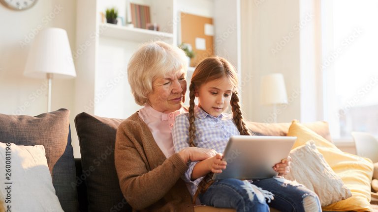 Großmutter und Kind sitzen auf dem Sofa und schauen gemeinsam auf ein Tablet.
