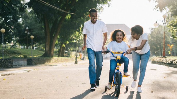 Little girl rides a bike and her parents help her - Family and work  