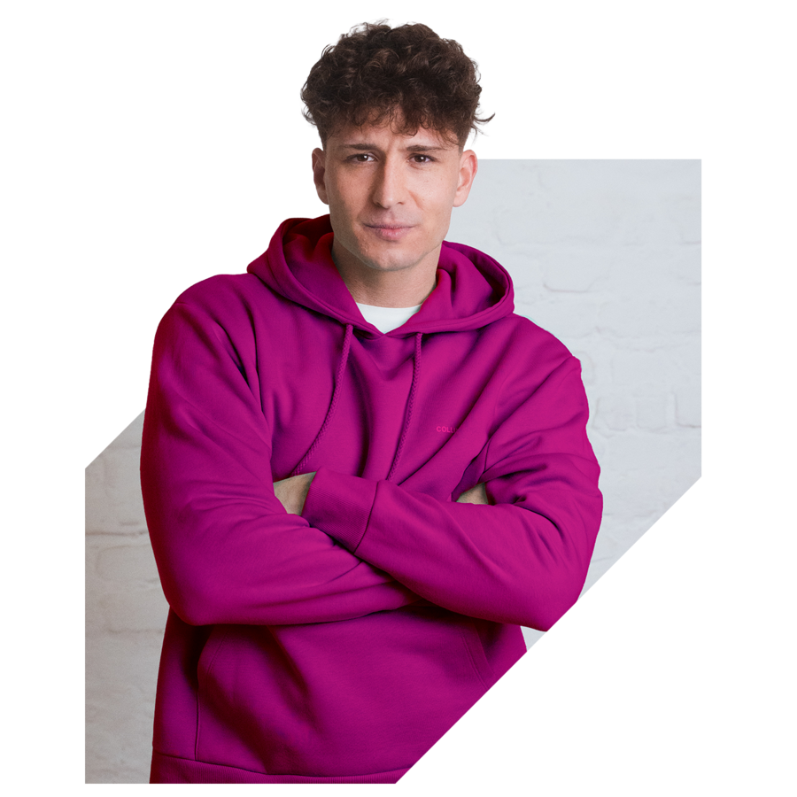 Junger Mann im pinken Hoodie steht mit verschränkten Armen vor hellem Hintergrund.