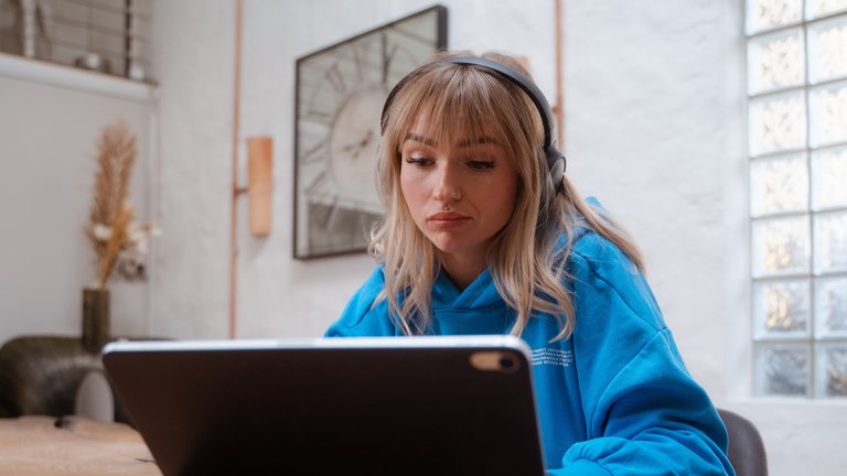 Junge Frau mit Kopfhörern arbeitet konzentriert an einem Tablet.