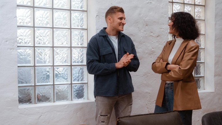 Zwei Personen unterhalten sich lächelnd vor einer Glasbausteinwand.