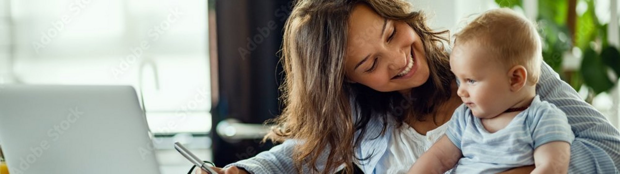 Eine Frau arbeitet am Laptop und hält ein Baby auf dem Arm