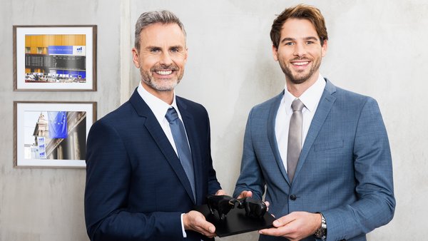 Zwei Männer im Anzug halten gemeinsam eine Skulptur von Bulle und Bär – steht symbolisch für Finanzmärkte und partnerschaftliche Zusammenarbeit.