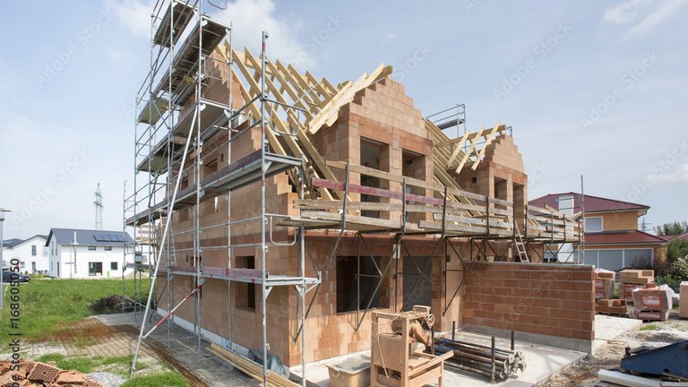 Rohbau eines Hauses mit Gerüst und Dachkonstruktion auf einer Baustelle.