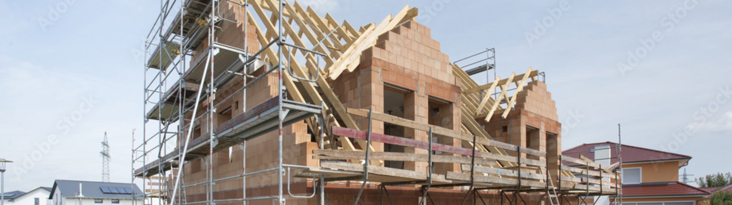 Rohbau eines Hauses mit Gerüst und Dachkonstruktion auf einer Baustelle.