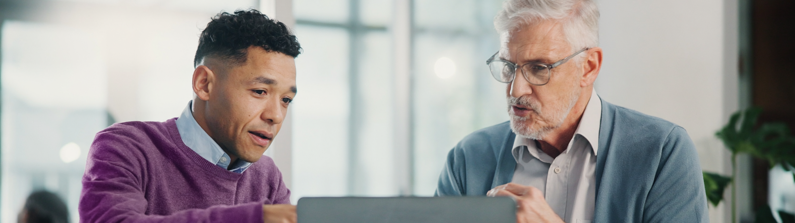 Zwei Männer schauen gemeinsam auf einen Laptop und besprechen etwas am Tisch.