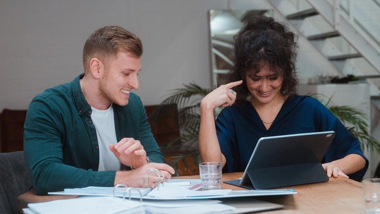 Zwei Personen arbeiten gemeinsam am Tisch mit Tablet und Unterlagen.