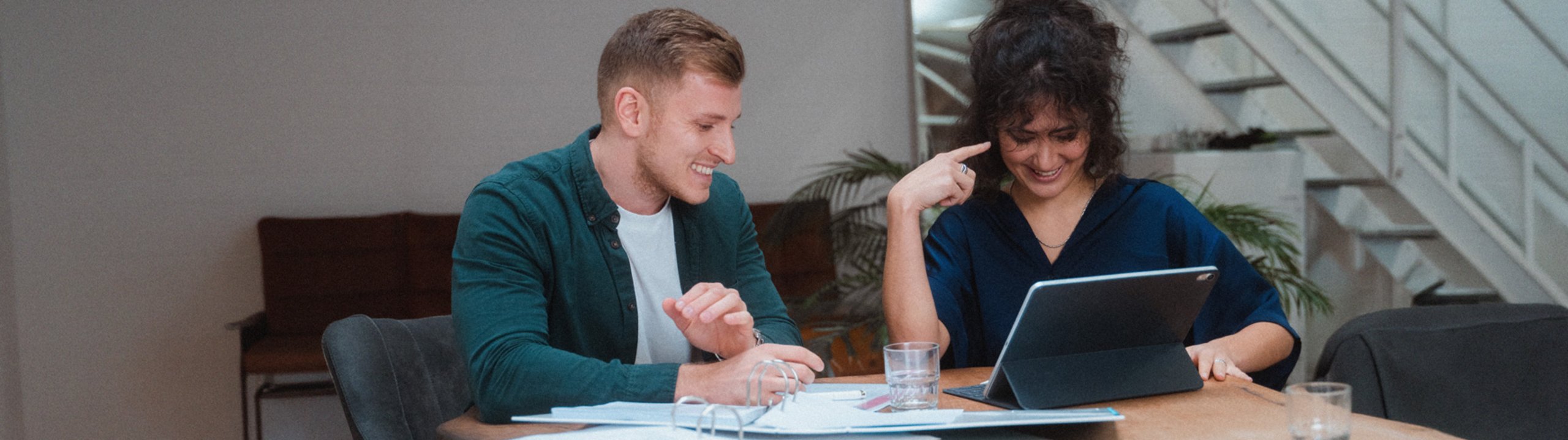 Zwei Personen arbeiten gemeinsam am Tisch mit Tablet und Unterlagen.