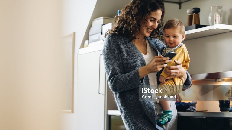 Eine Person hält ein Kleinkind auf dem Arm und schaut gemeinsam mit ihm auf ein Smartphone in einer modernen Küche.