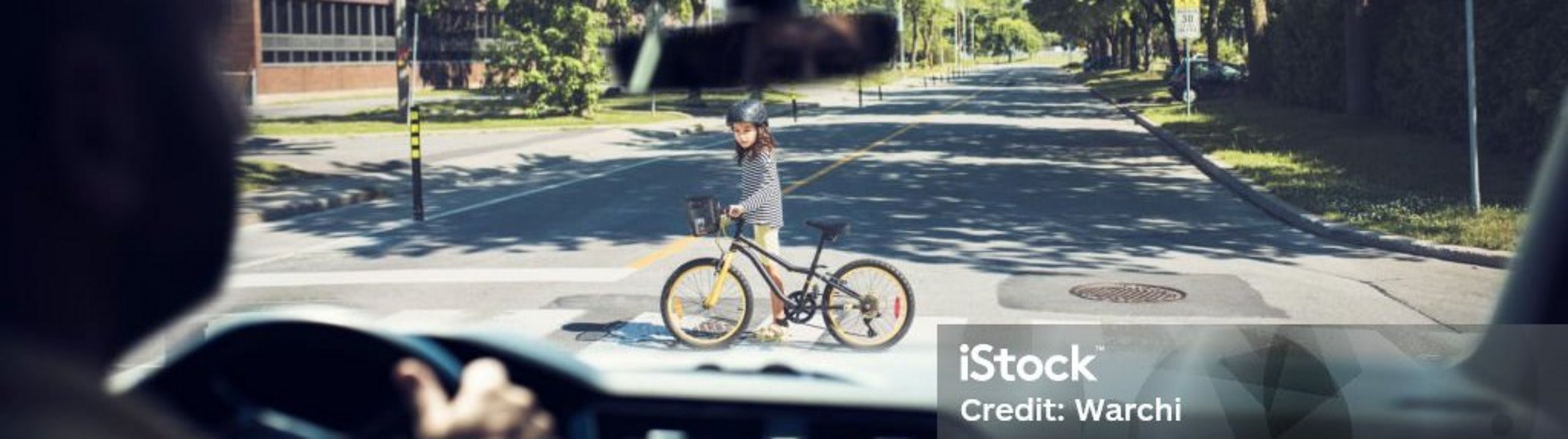 Kind überquert mit einem Fahrrad die Straße, gesehen aus einem Auto.