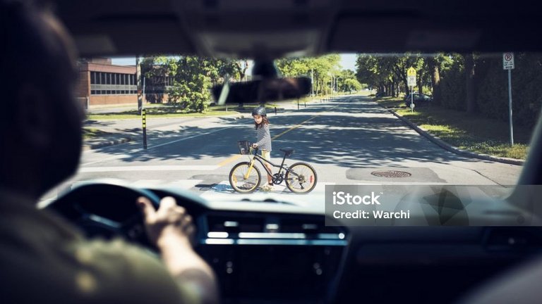 Kind überquert mit einem Fahrrad die Straße, gesehen aus einem Auto.