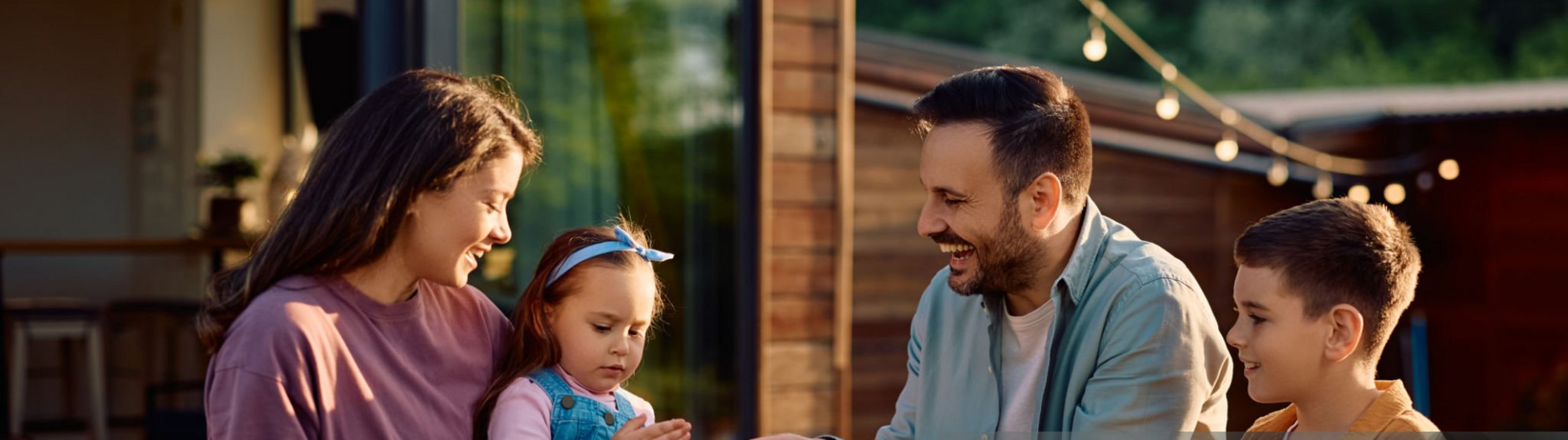 Eine Familie mit zwei Kindern sitzt gemeinsam an einem gedeckten Tisch auf der Terrasse und genießt entspannt das Essen.