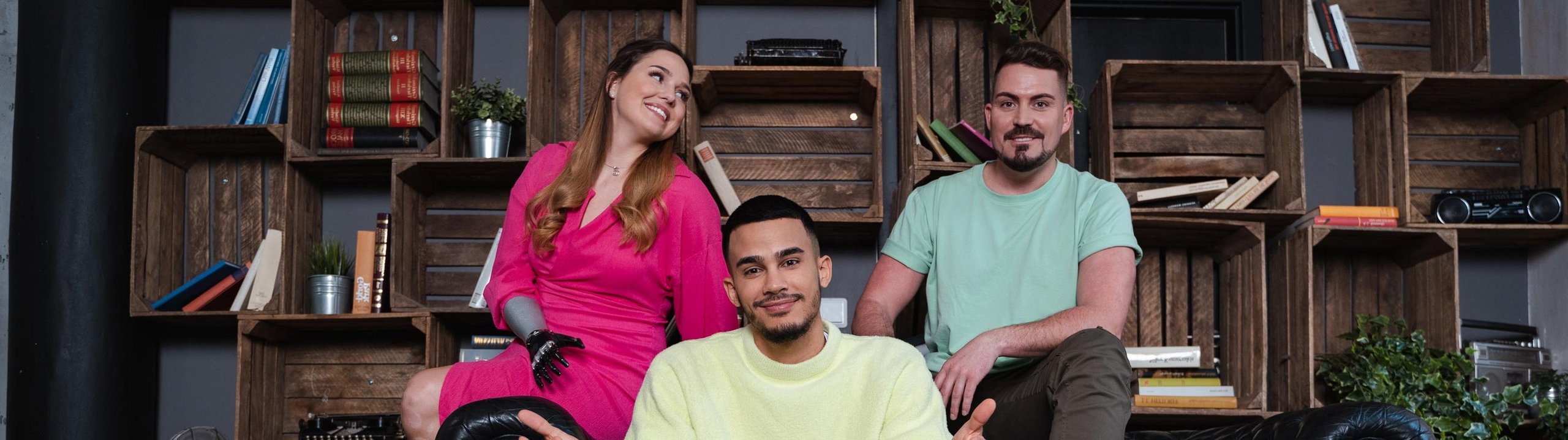 Drei Personen sitzen entspannt auf einem Sofa vor einem Bücherregal.