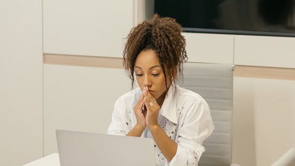 Young woman sitting and pondering in front of a laptop – resilience 