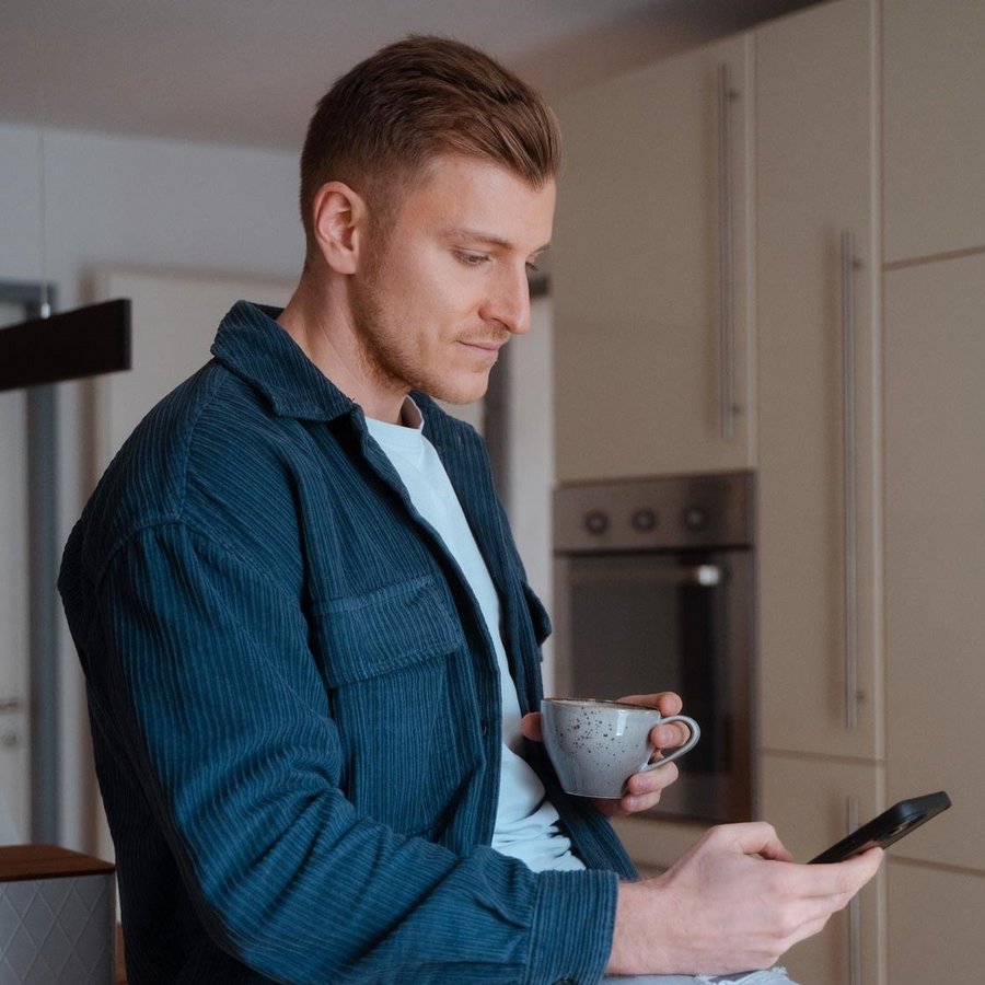 Mann sitz in der Küche und schauts auf sein Handy
