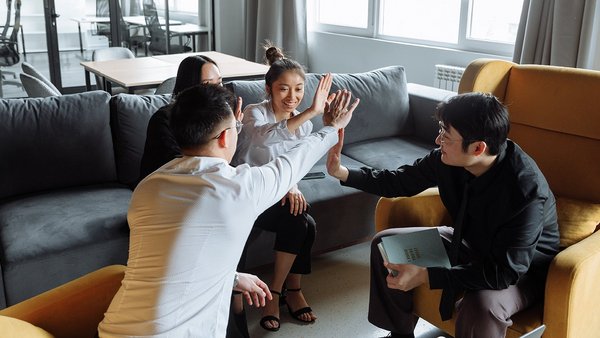 Vier junge Menschen im Teammeeting geben sich ein High five Vier junge Menschen im Teammeeting geben sich ein High five