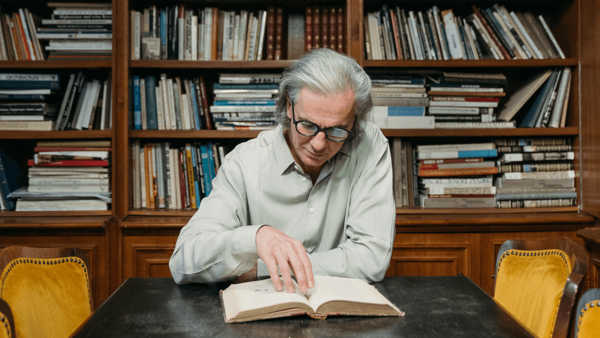 Älterer Mann sitzt in einer Bibliothek und liest ein Buch – Silver Society 