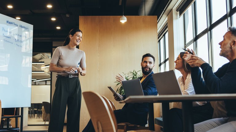 Meeting im Büro: Eine Frau präsentiert, während andere am Tisch zuhören und diskutieren.