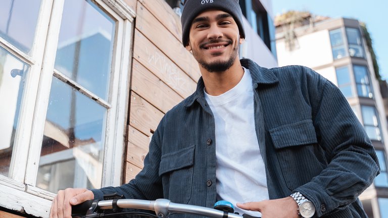 Mann mit Mütze steht lächelnd neben seinem Fahrrad.
