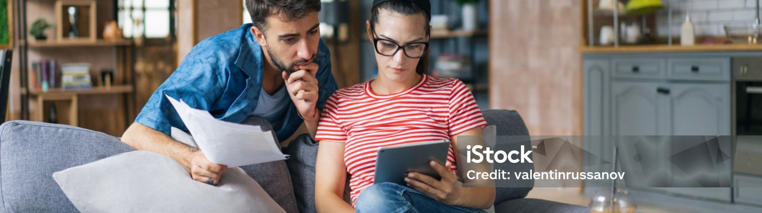 Paar sitzt am Tablet mit Unterlagen in der Hand