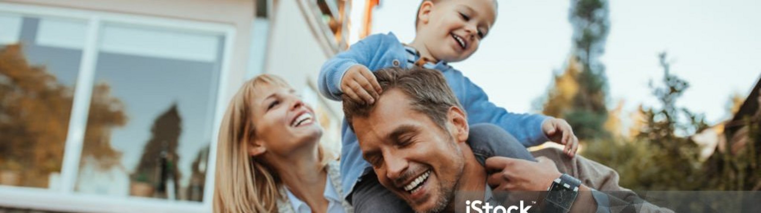Familie spielt lachend im Garten, Kind sitzt auf den Schultern des Vaters.