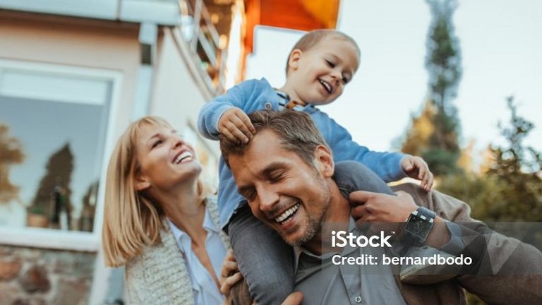 Familie spielt lachend im Garten, Kind sitzt auf den Schultern des Vaters.