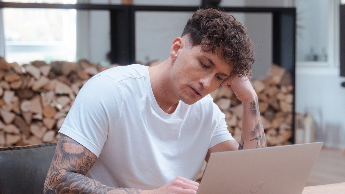 A young man is sitting in front of his laptop while feeling sick.