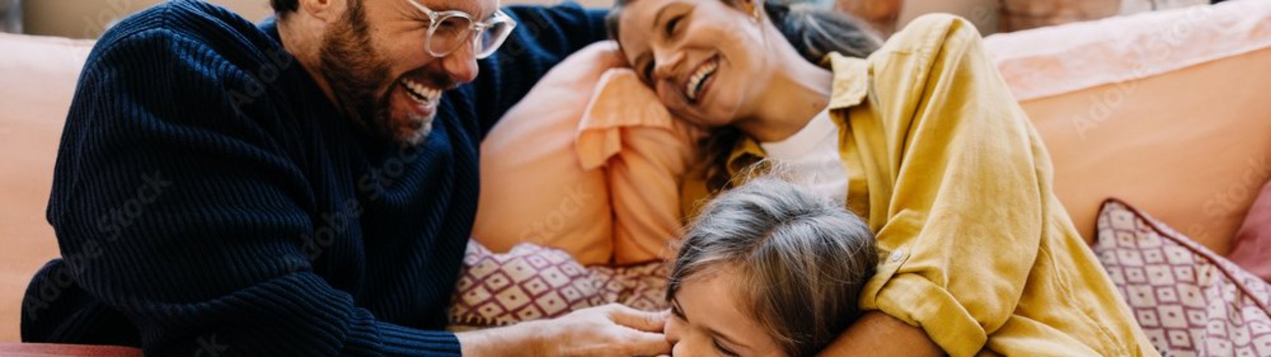 Familie kuschelt lachend auf dem Sofa.