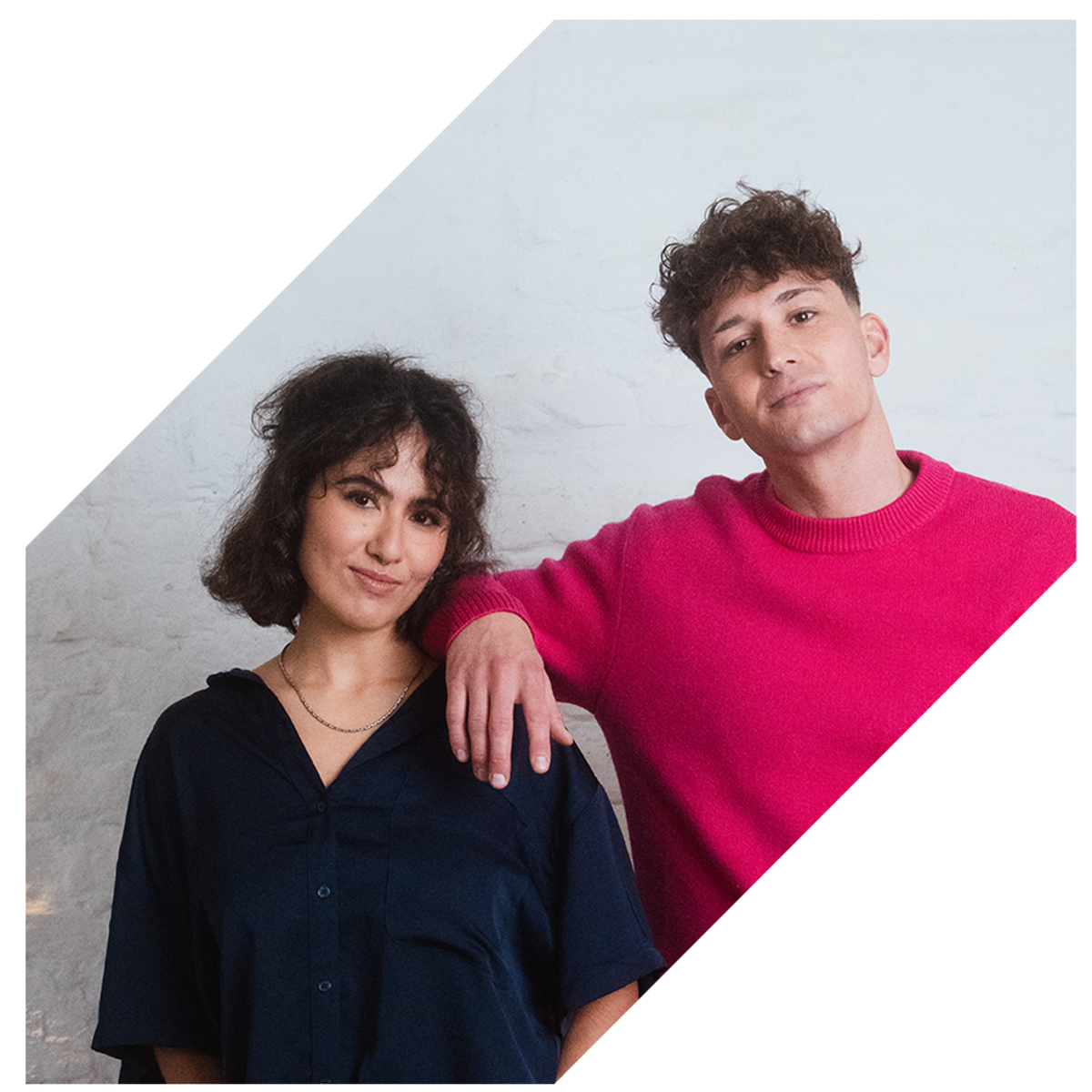 Zwei junge Erwachsene stehen entspannt nebeneinander vor hellem Hintergrund.