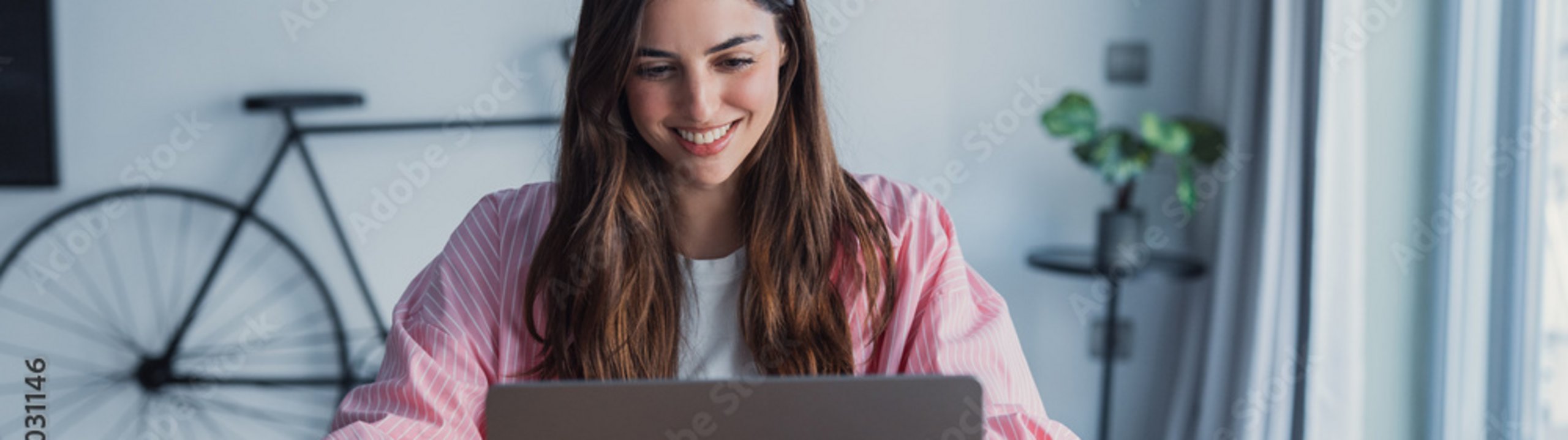 Eine lächelnde Person arbeitet an einem Laptop an einem Holztisch im Homeoffice.