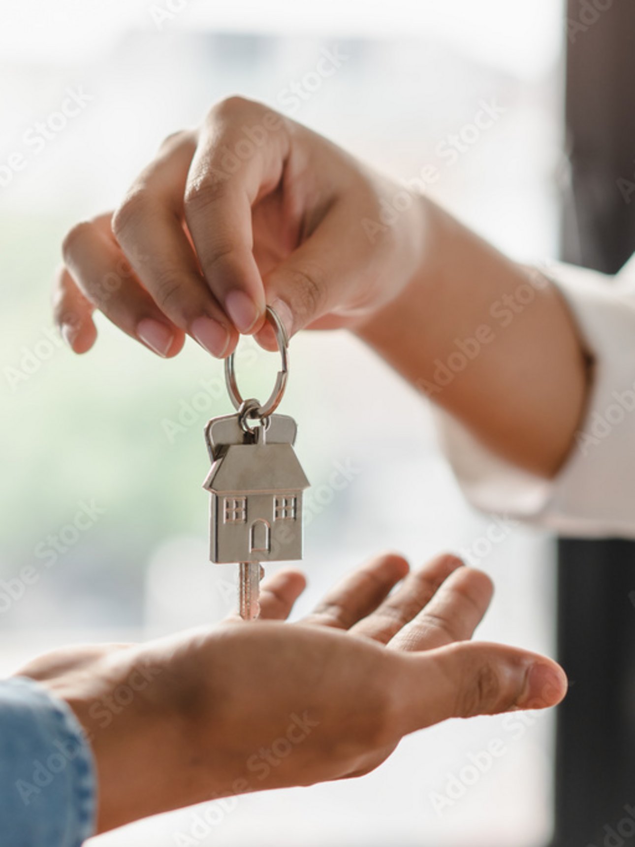 Eine Person übergibt einer anderen einen Hausschlüssel mit Haus-Anhänger.