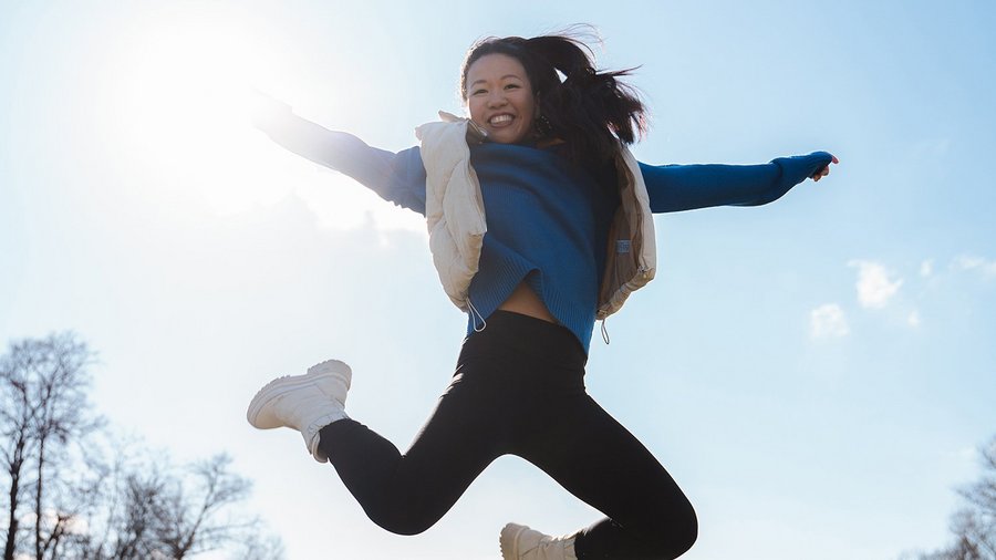 Frau springt mit ausgebreiteten Armen in den Himmel