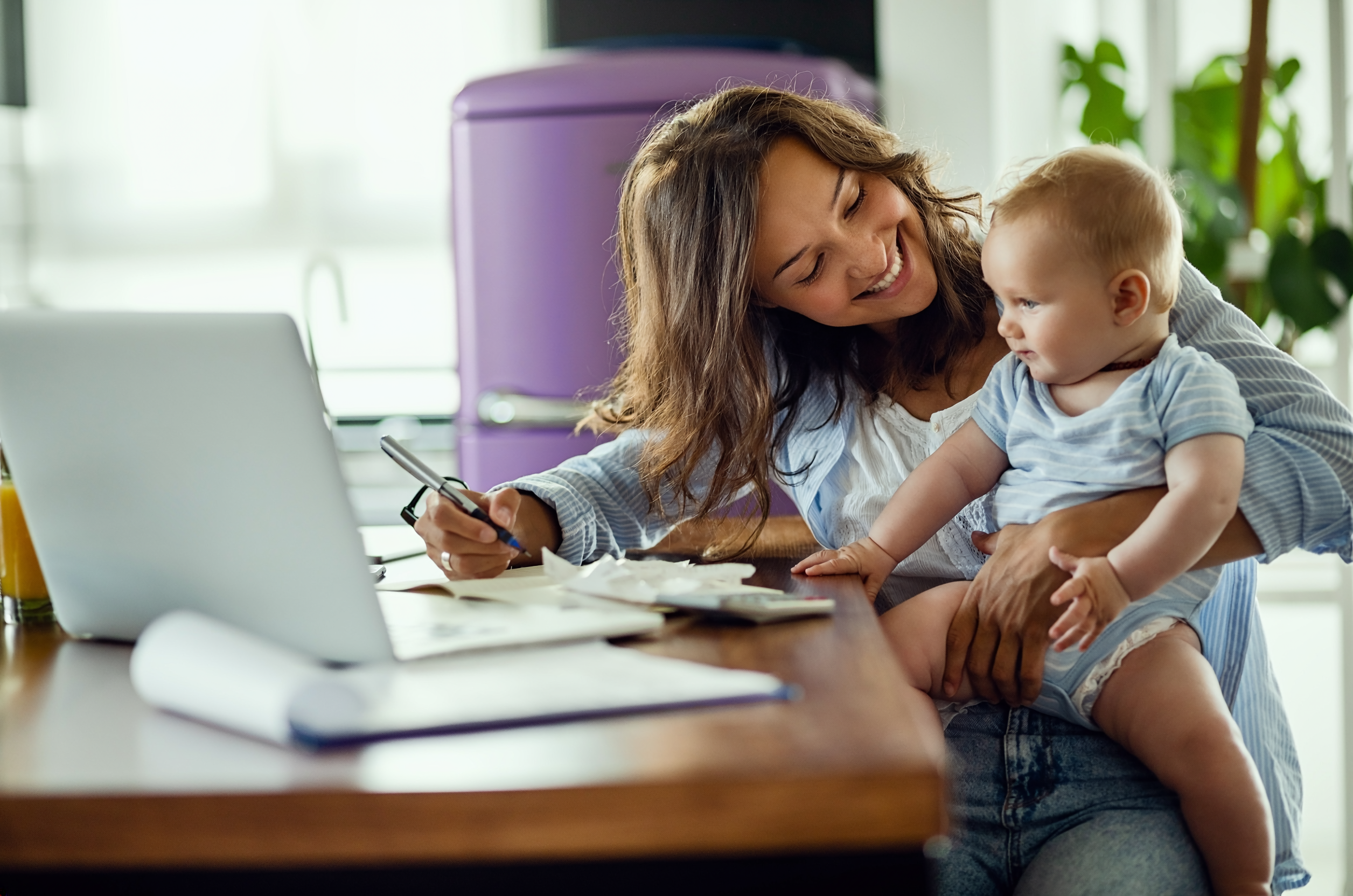 Eine Frau arbeitet am Laptop und hält ein Baby auf dem Arm