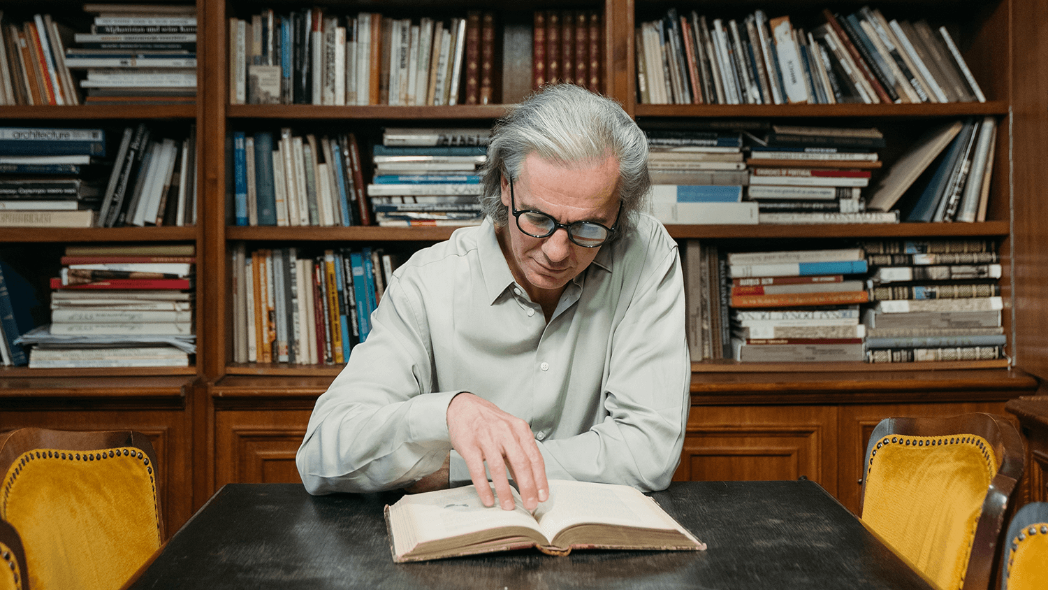 Älterer Mann sitzt in einer Bibliothek und liest ein Buch – Silver Society Älterer Mann sitzt in einer Bibliothek und liest ein Buch – Silver Society