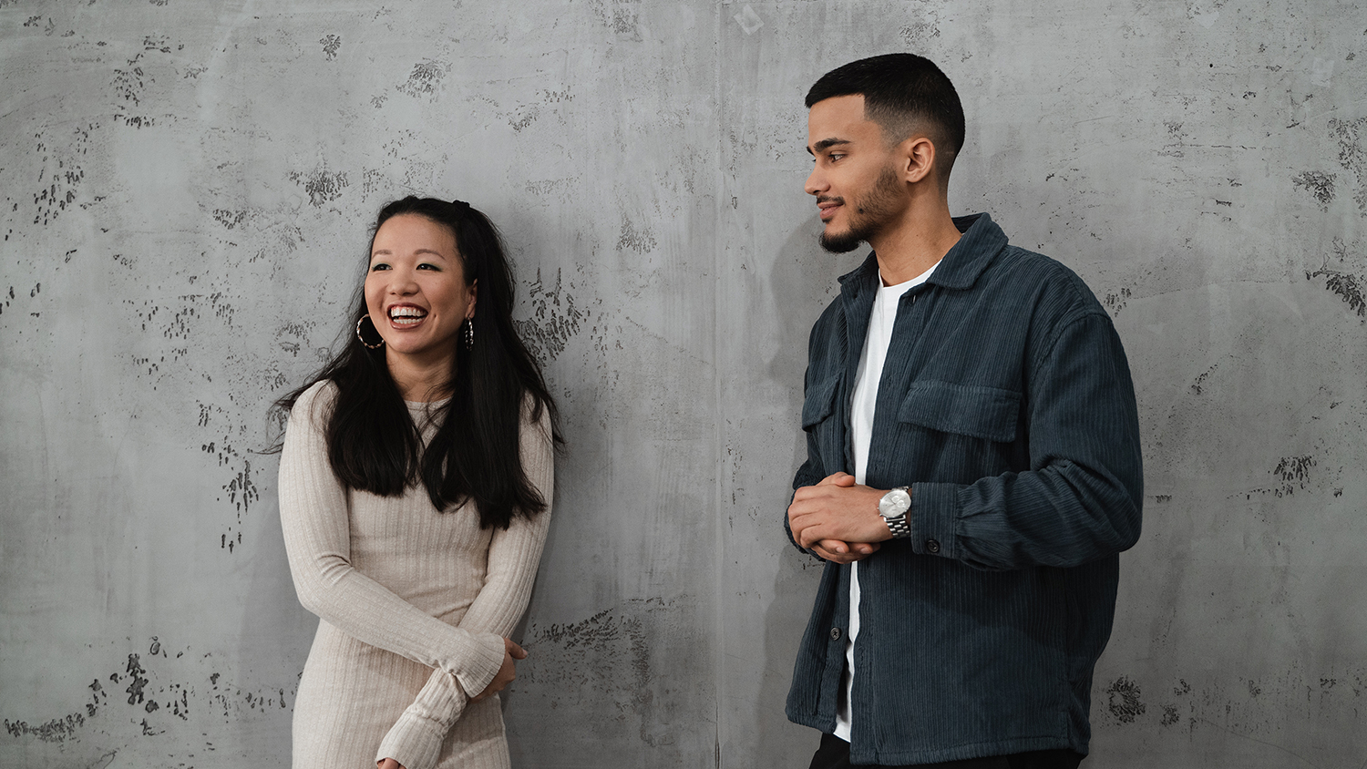 Man and woman laughing next to each other in front of a wall