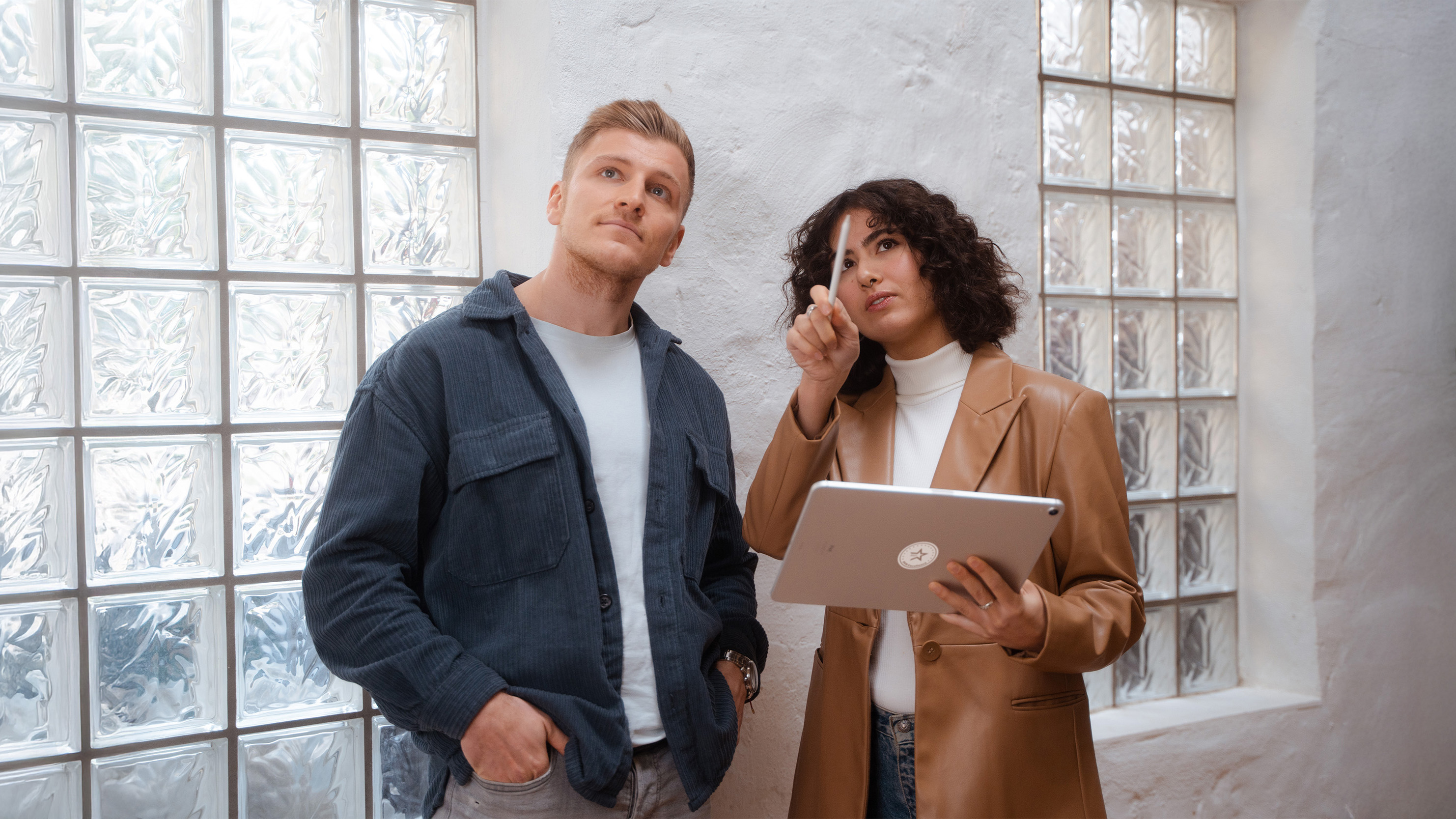 Two people are standing by a wall with a window and looking up.