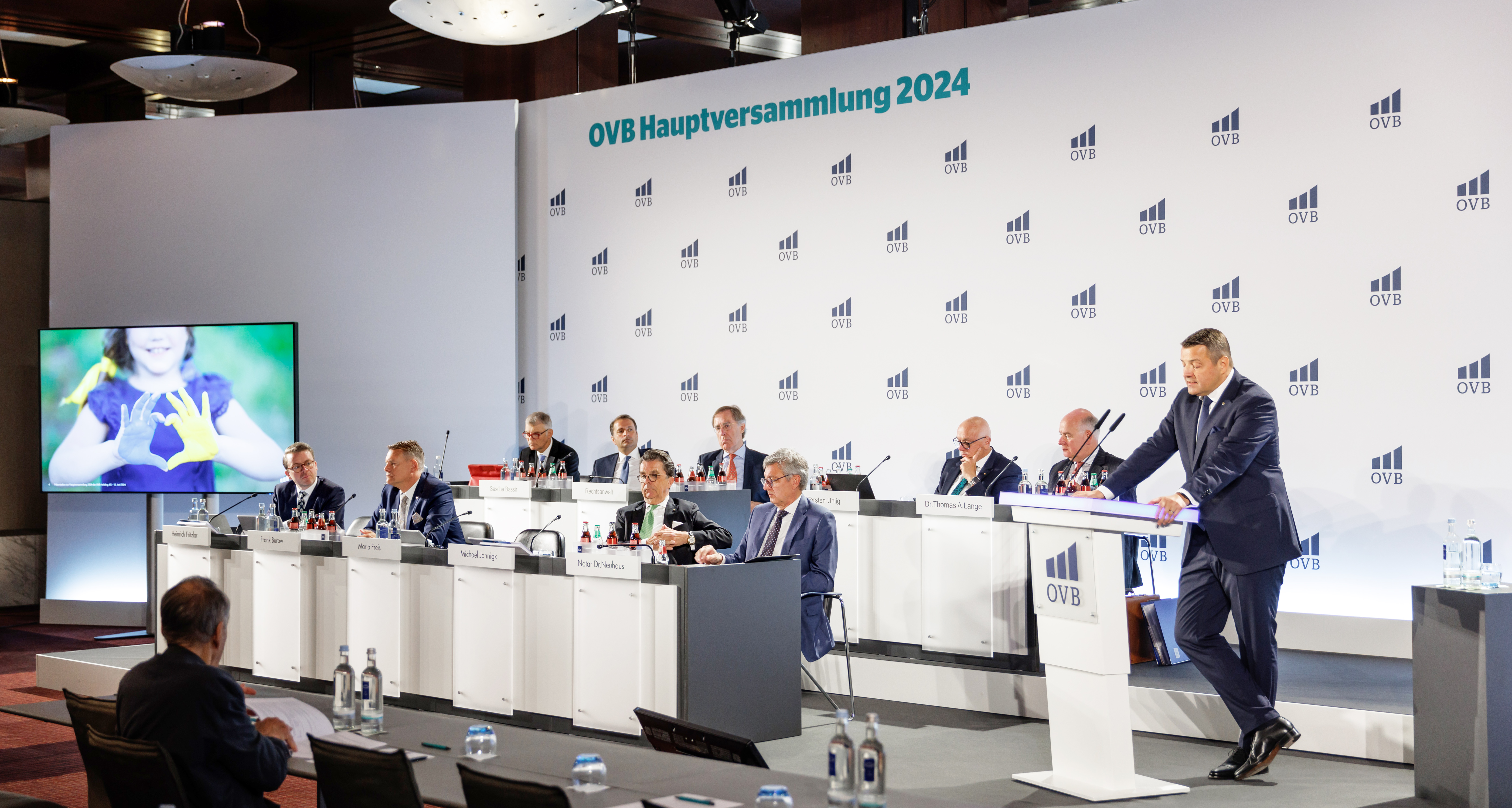 Podium mit mehreren Vorstandsmitgliedern bei der OVB Hauptversammlung 2024, der CEO Mario Freis steht am Rednerpult.