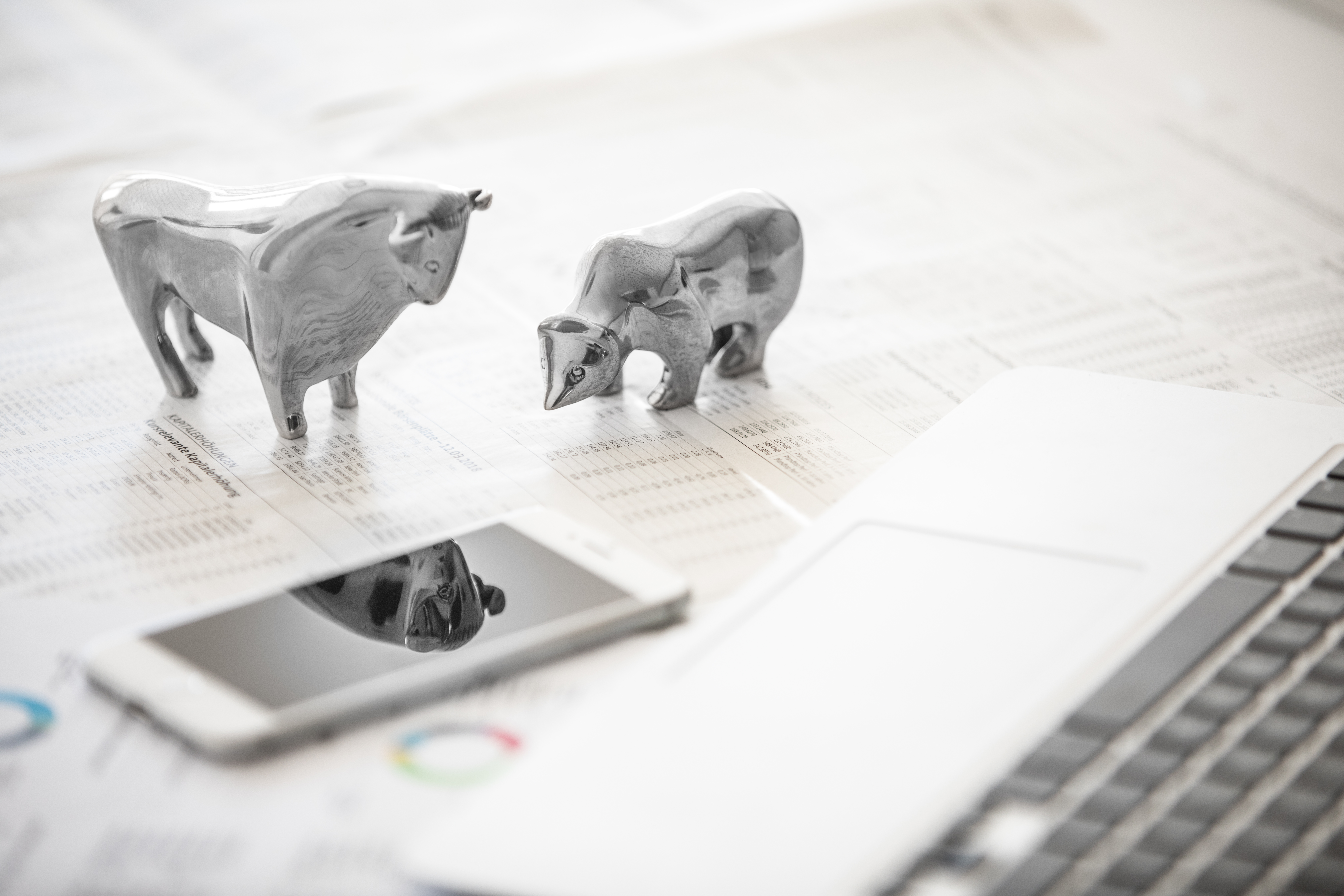 Foto von silbernen Bulle und Bär Figuren auf einem Tisch neben einem Smartphone
