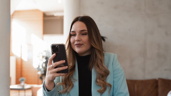 Frau im Blazer schaut lächelnd auf ihr Handy.