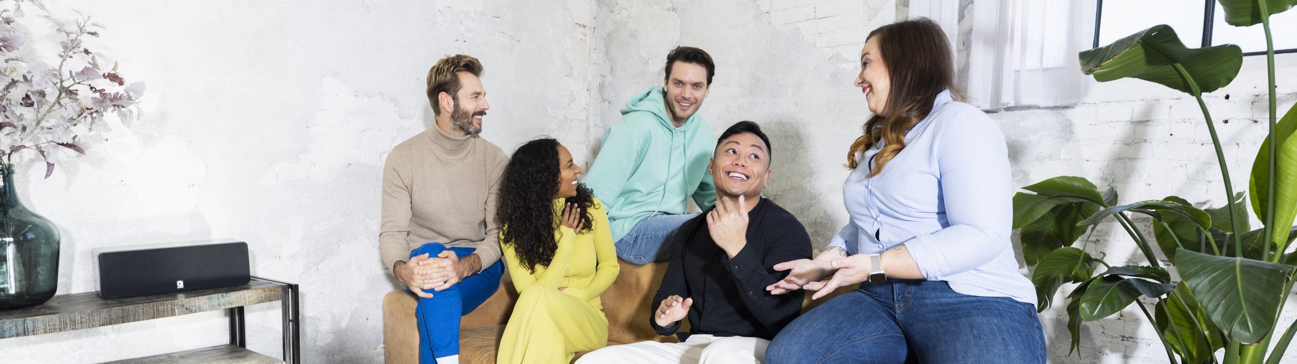 Eine Gruppe von fünf Personen sitzt gemeinsam auf einem Sofa und unterhält sich lachend.