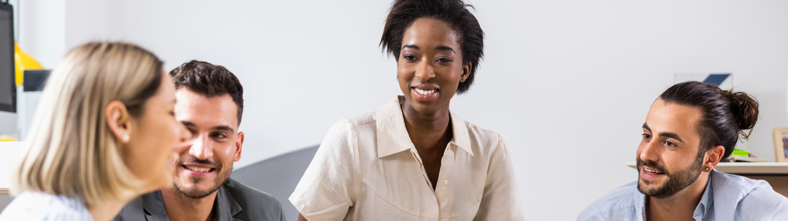 Diverse Gruppe junger Berufstätiger im Gespräch in einem modernen Büro, symbolisiert Zusammenarbeit und Teamgeist.