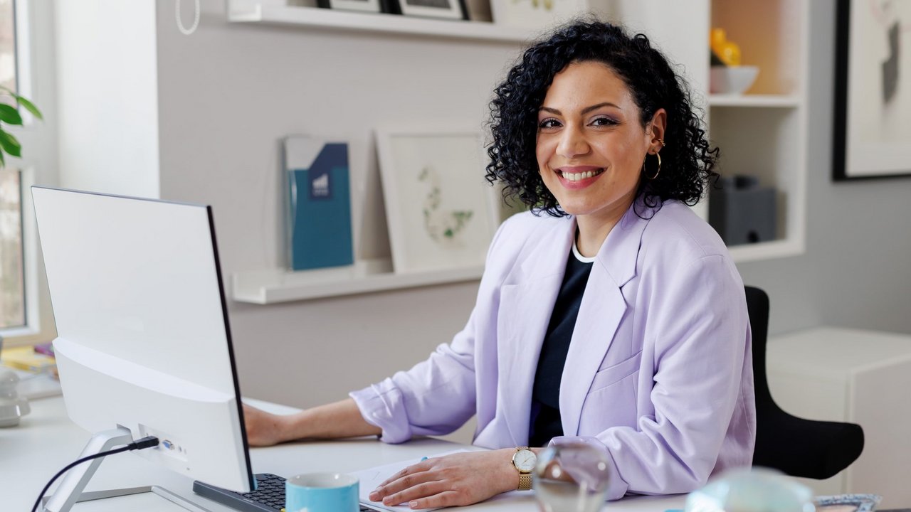 A young woman smiles and looks over her shoulder. Behind her, two other people can be seen sitting at a table.