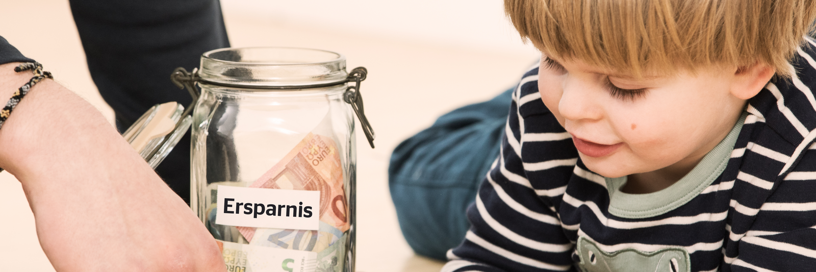 [Translate to english:] Kleiner Junge spielt neben Glas mit finanziellen Ersparnissen
