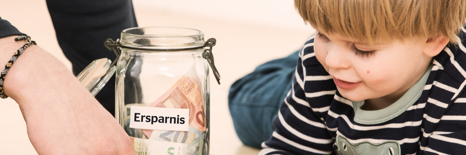 Kleiner Junge spielt neben Glas mit finanziellen Ersparnissen