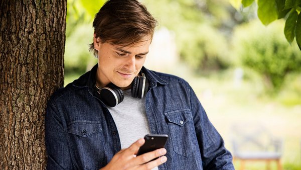 Young man leaning against tree with smartphone 