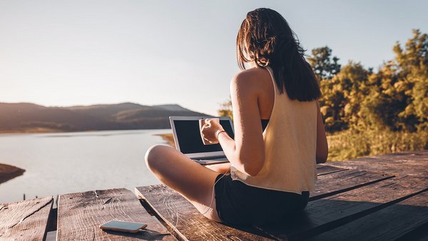 Mobiles Arbeiten im Ausland – Frau sitzt mit Laptop am See 